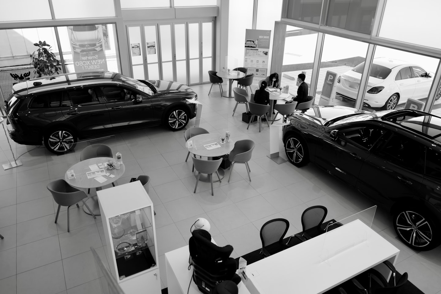 Customers discuss papers at tables in a modern car dealership showroom.